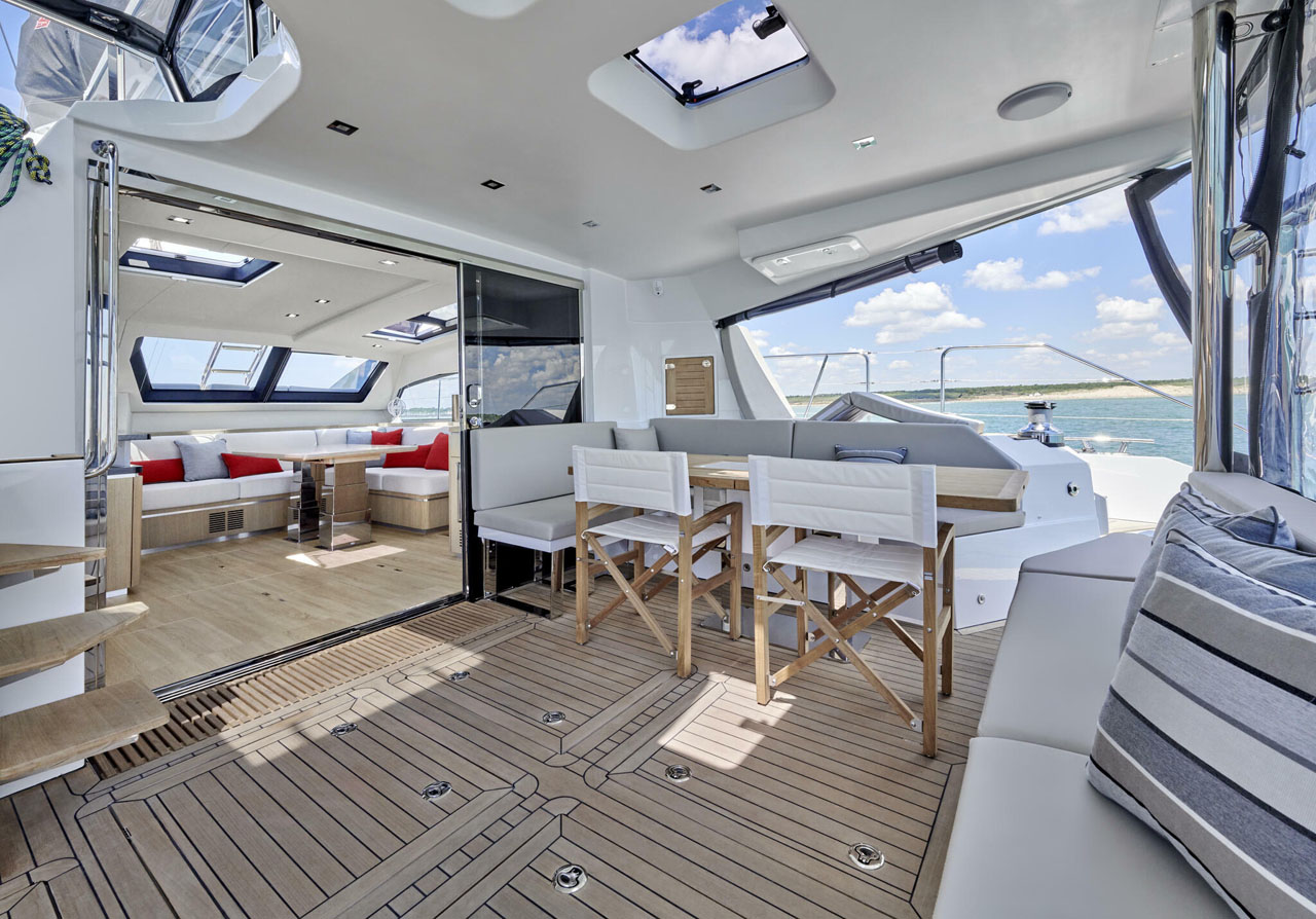 Luxurious yacht deck with dining area, modern interior, and ocean view under a clear blue sky.
