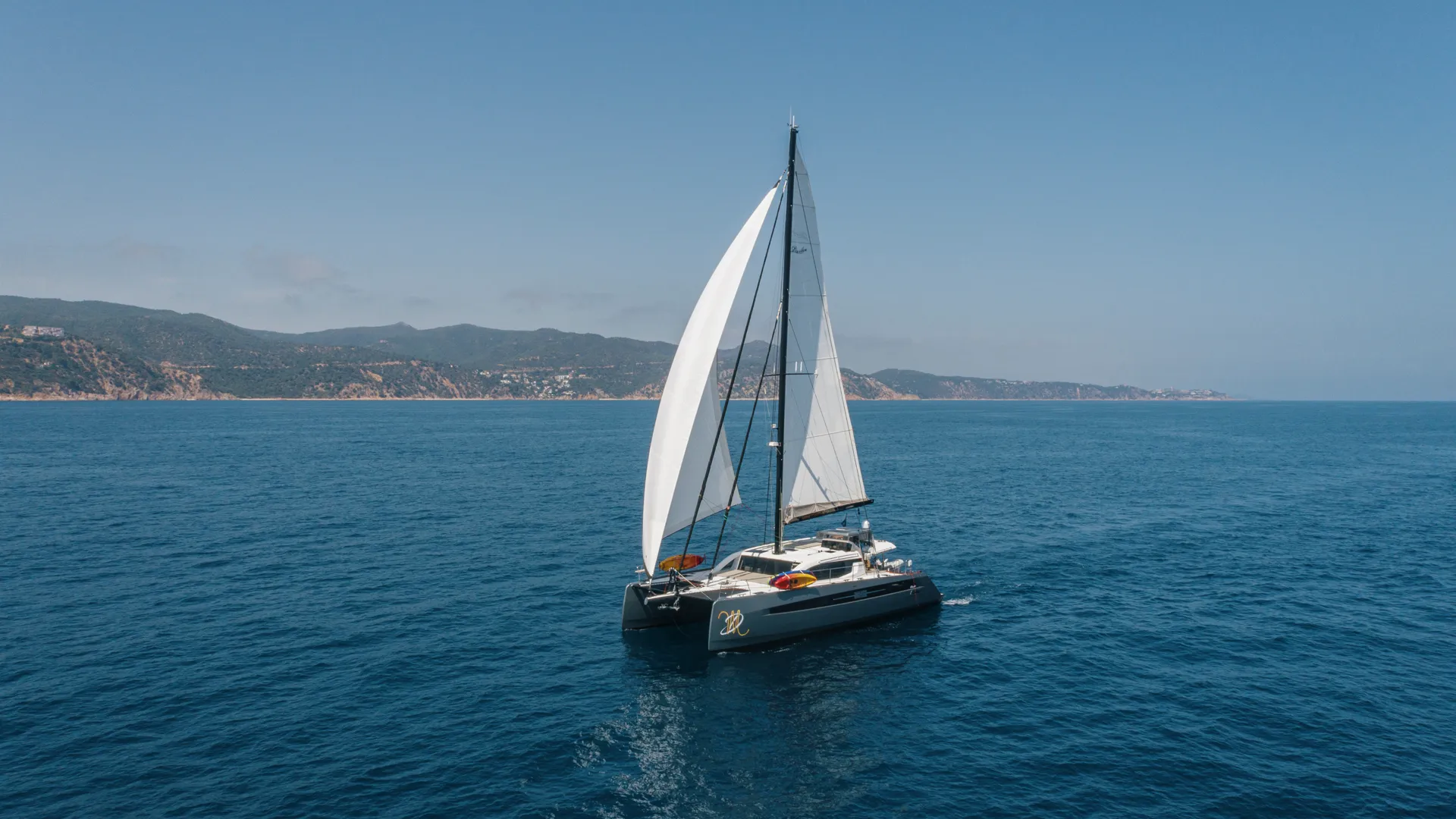 Privilege signature 580 Sailing catamaran on open sea with scenic coastal background under clear blue sky.
