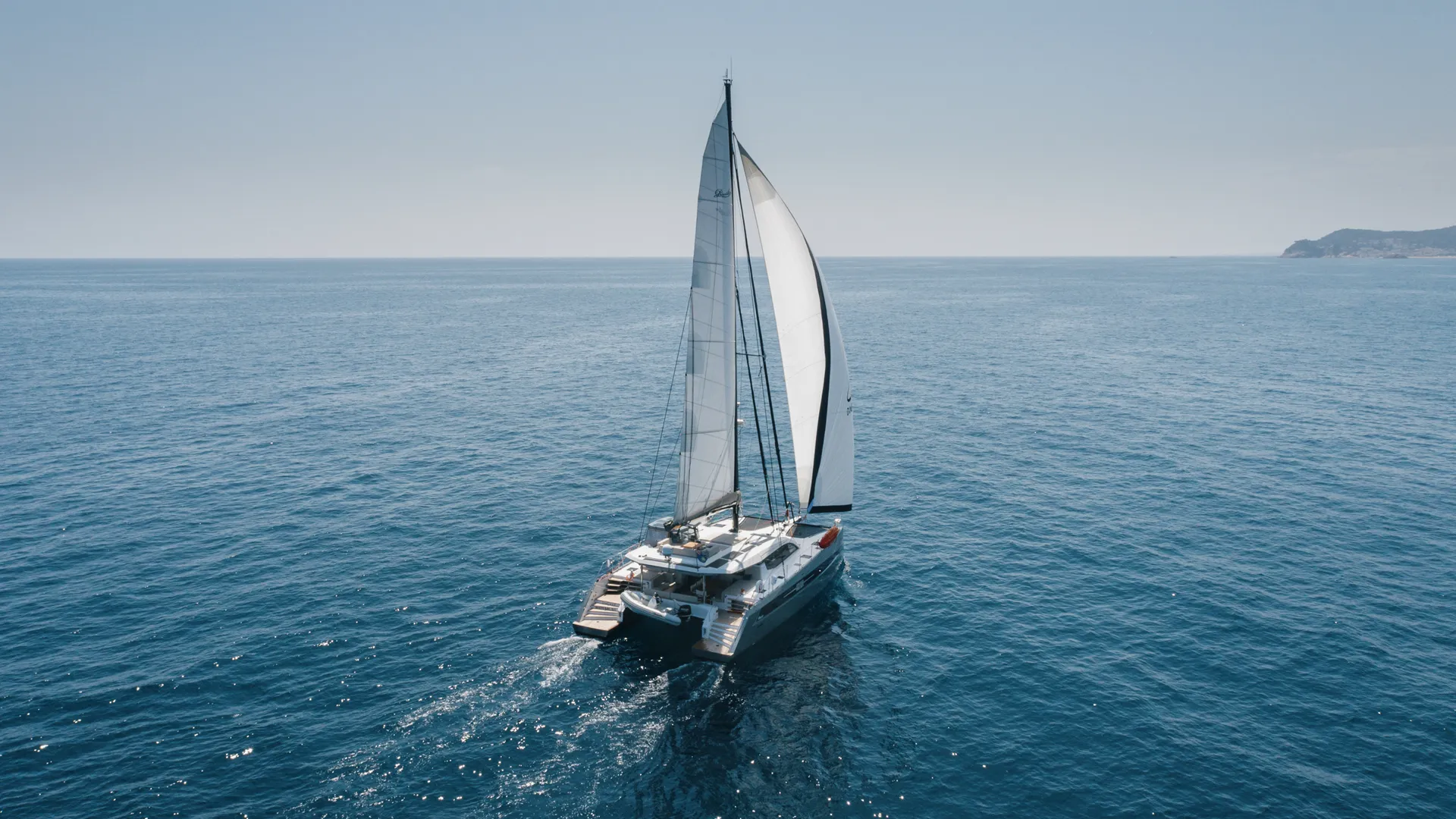 Sailing catamaran gliding on the open sea under clear skies.